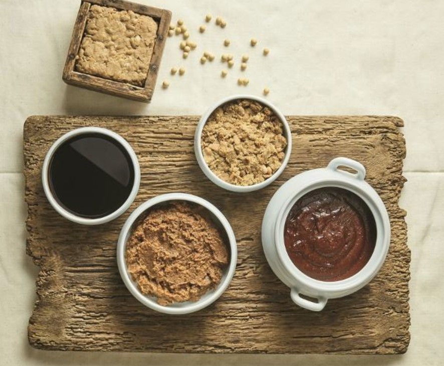 Ganjang, Doenjang und Gochujang in Schalen, daneben Sojabohnen und ein Meju-Block