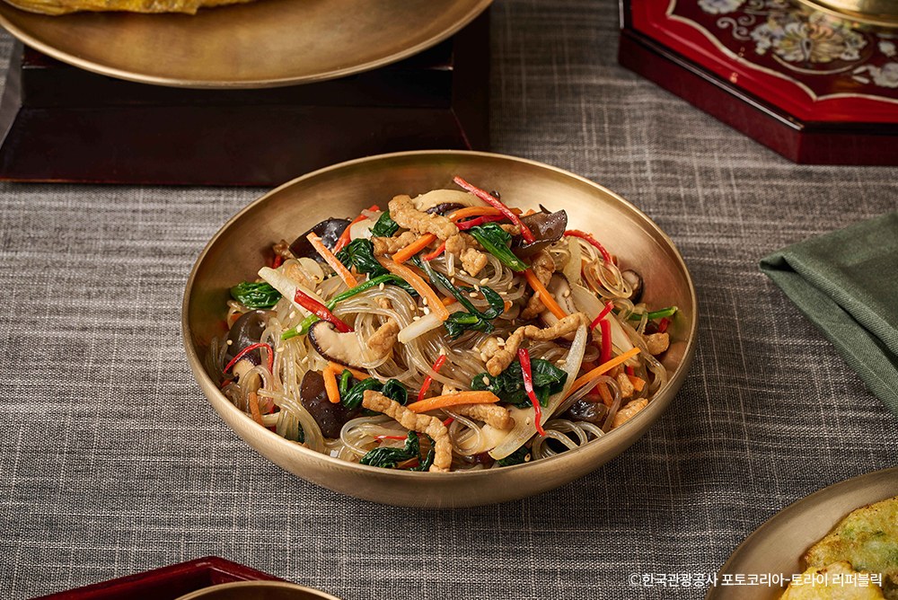 Traditionelles Japchae mit Karotte, Spinat und Pilzen in einer Messingschüssel
